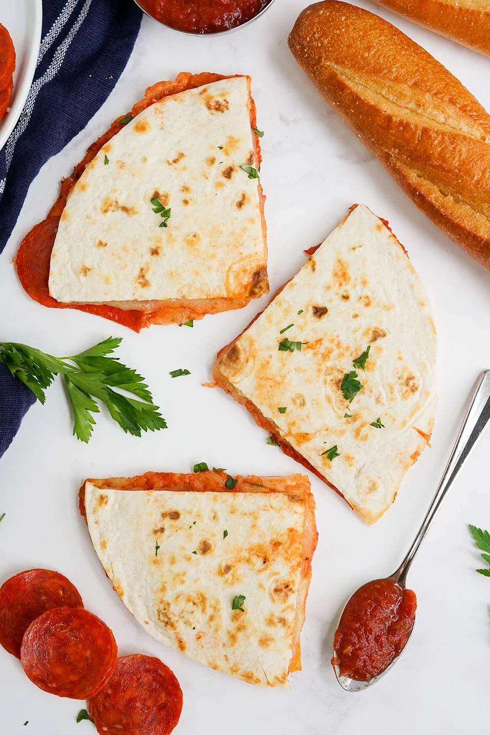 Overhead image of quesadilla slices next to bread, sauce, and pepperoni slices.