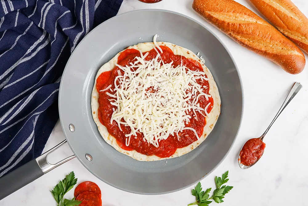 Shredded mozzarella on top of a sauced tortilla in a skillet. 