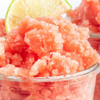 Watermelon granita in a clear cup with a slice of lime on top.