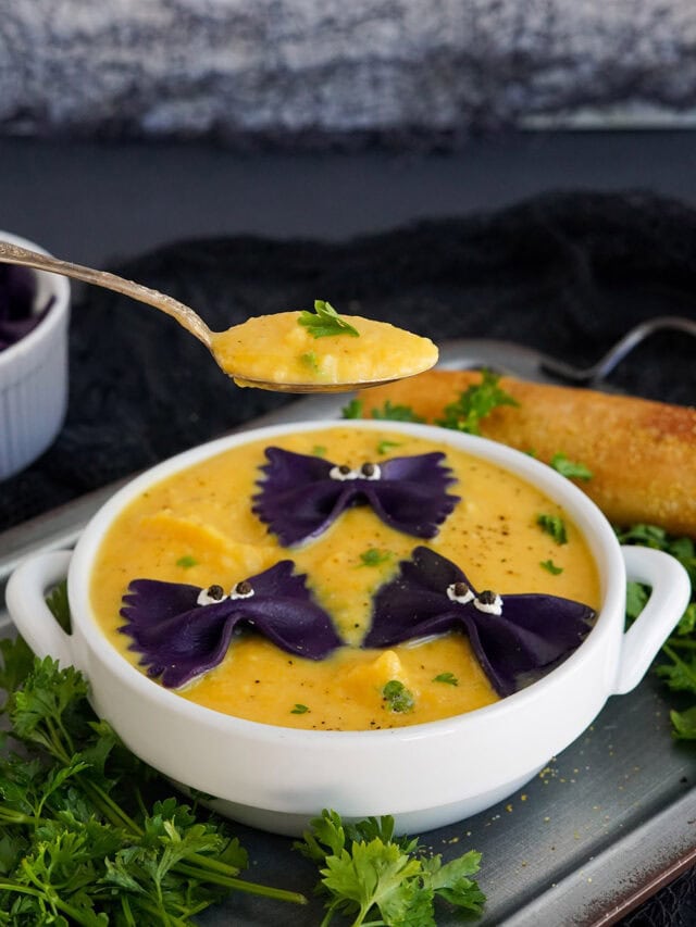 Raised spoon with butternut squash soup with bowl in the background.