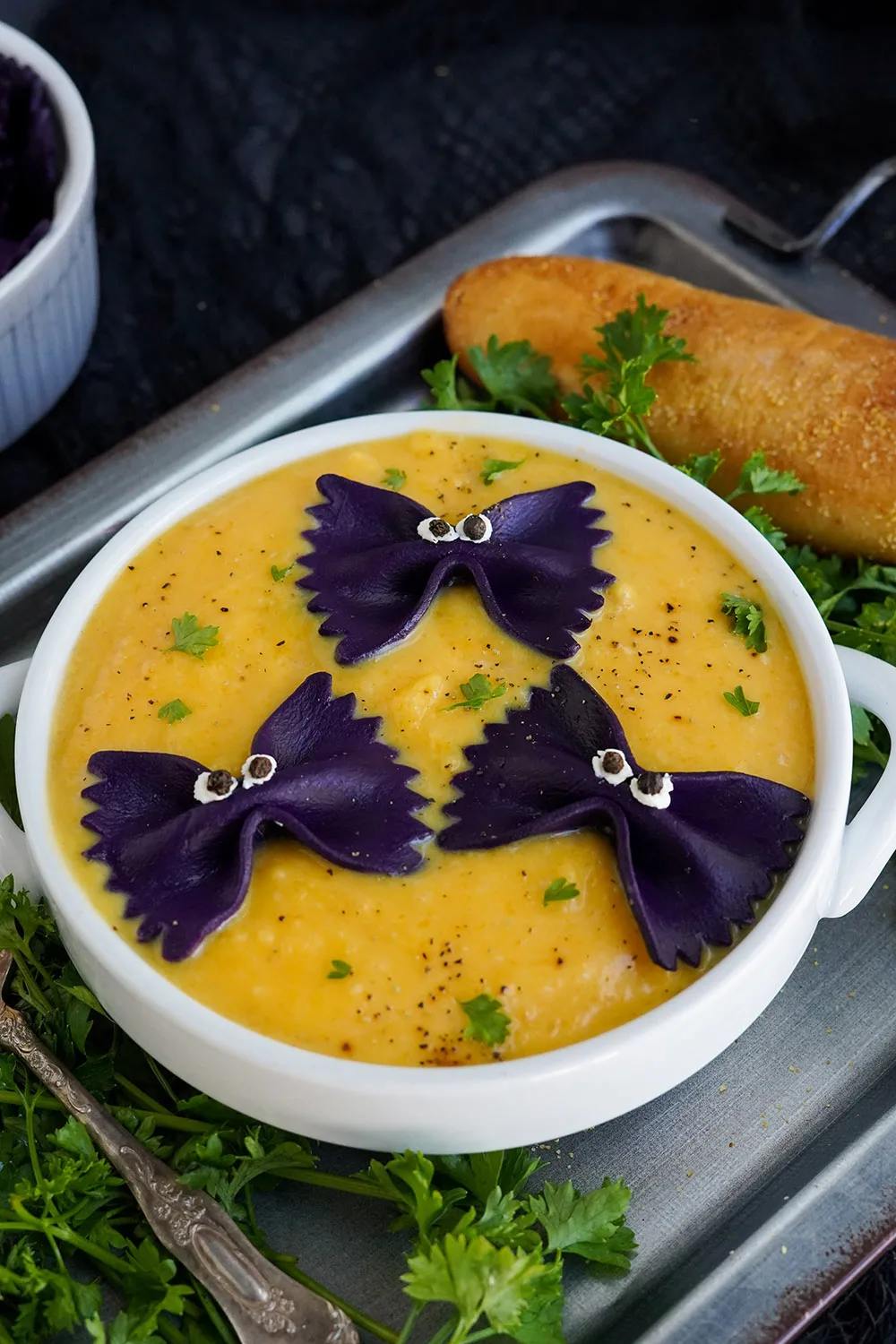 Bowl of soup with pasta bats with eyes with bread next to it on a baking sheet.