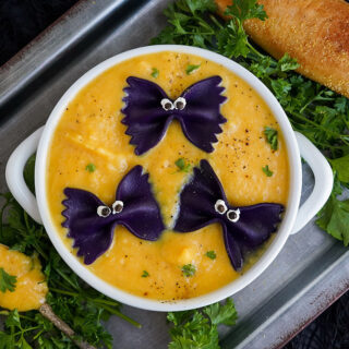 Bowl of soup on top of a pan. Black pasta tops the butternut squash soup.