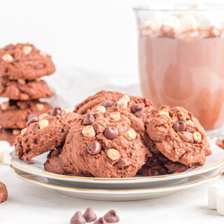 Stacked hot cocoa cookies next to a mug and a plateful of cookies.