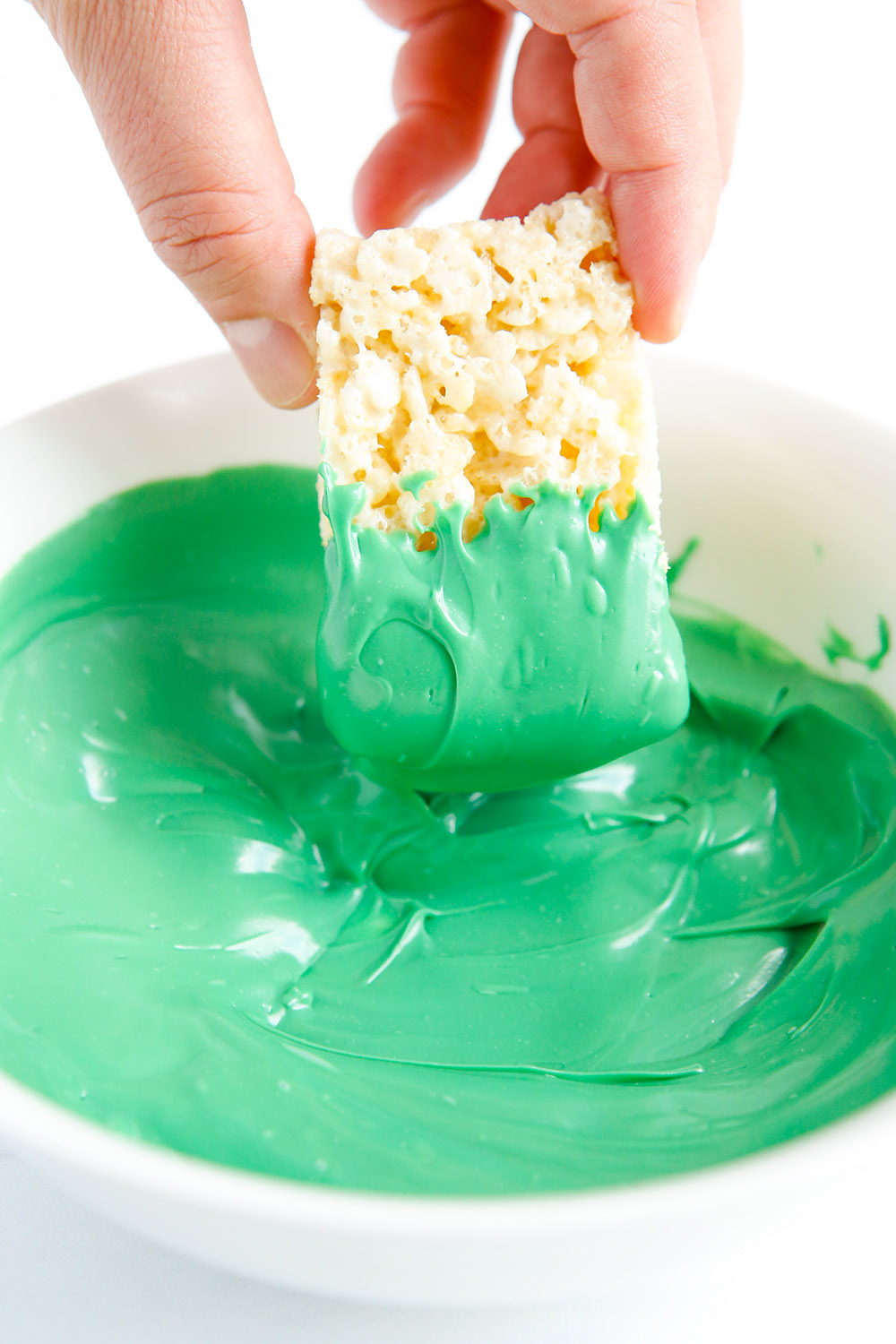Dipping a rice crispy treat into melted green candy. 