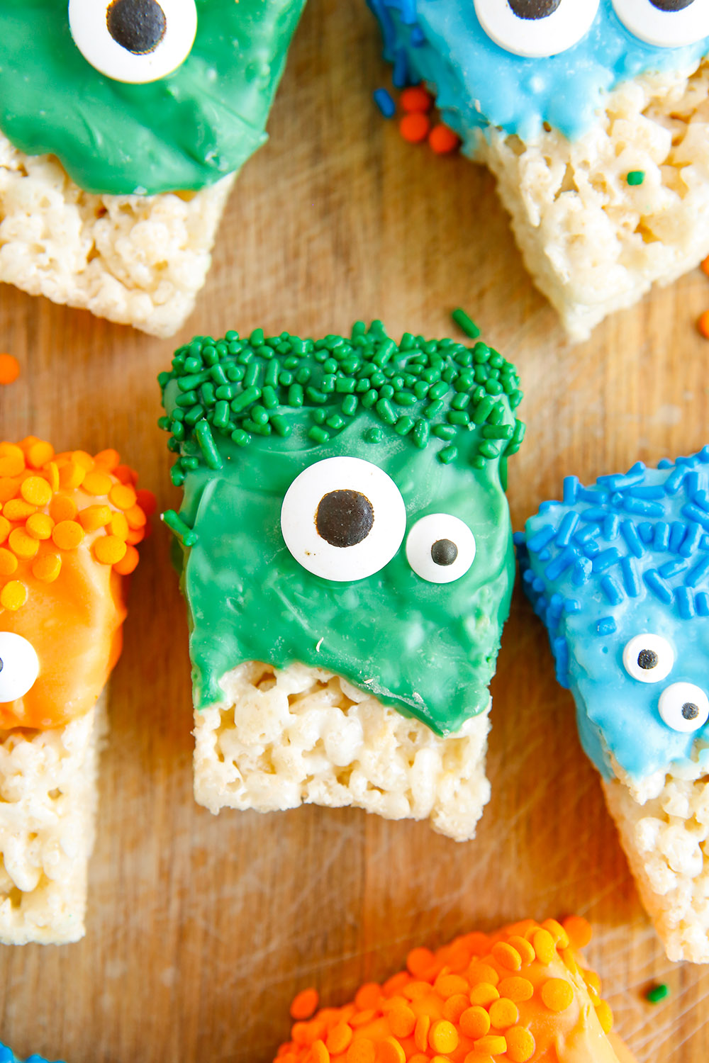 Green, blue, and orange candy melts on rice crispy treats with eyes for Halloween monsters. 