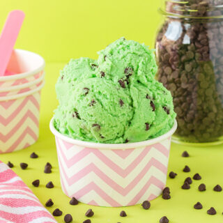 Scoops of mint chip cookie dough in a pink striped cup with chips on the table.