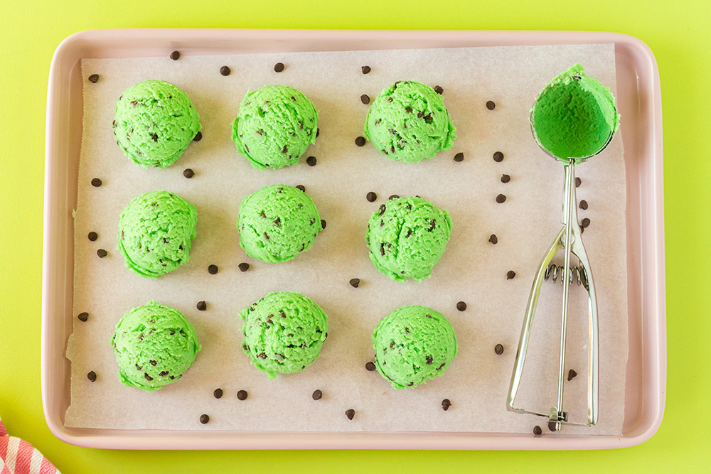 Scoops of mint chocolate chip cookie dough on a baking sheet. 