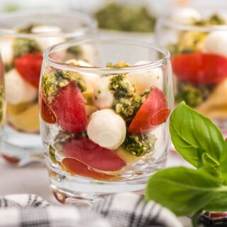 Glasses with pasta, pesto, tomatoes, and mozzarella for salad shooters.