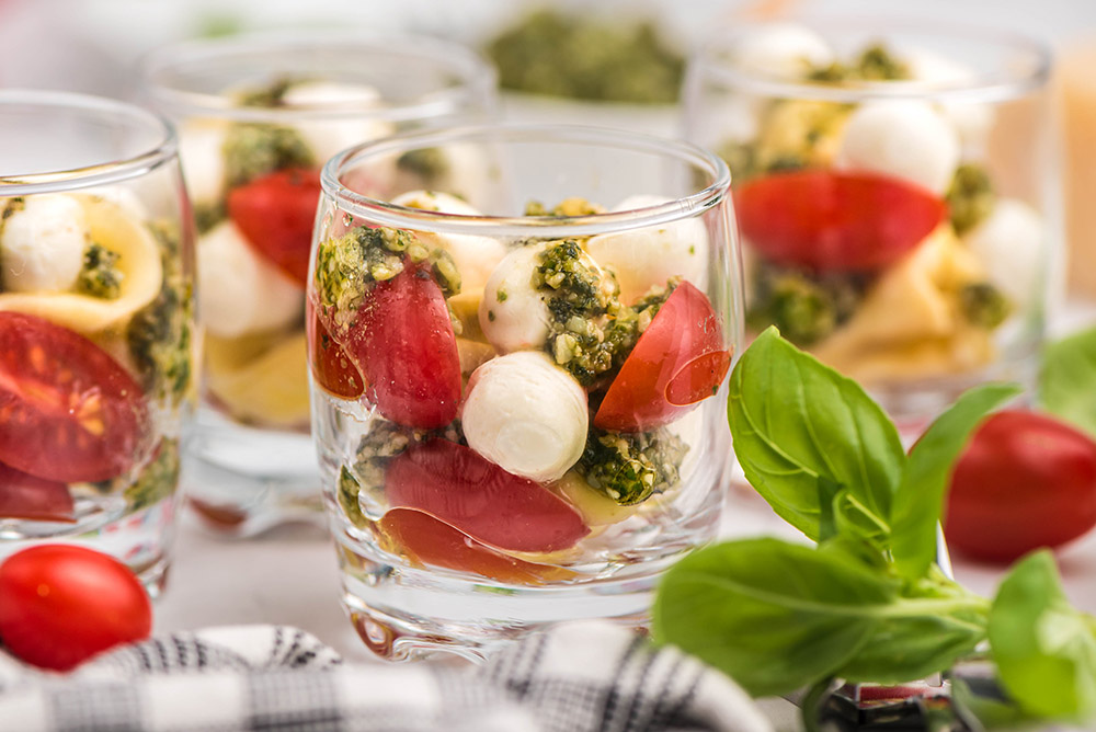 Glasses with pasta, pesto, tomatoes, and mozzarella for salad shooters.