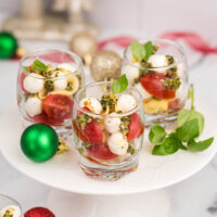 Glasses of tomato, mozzarella, pesto salad with holiday ornaments on the table.
