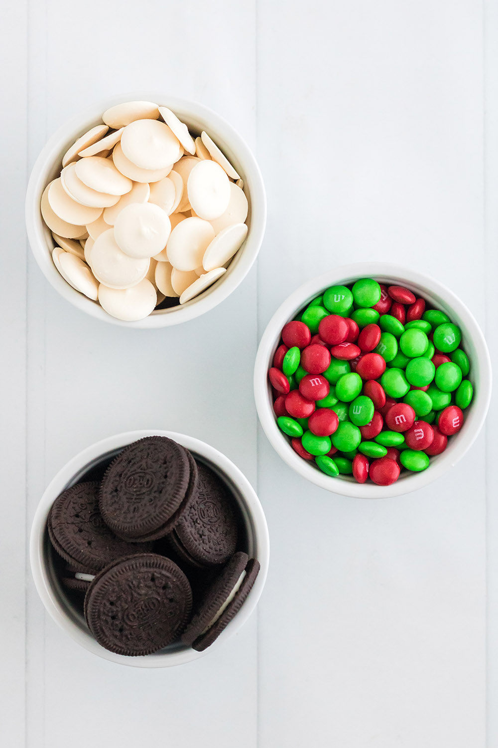 White candy melts, OREO cookies, and red and green M&M candies in bowls. 