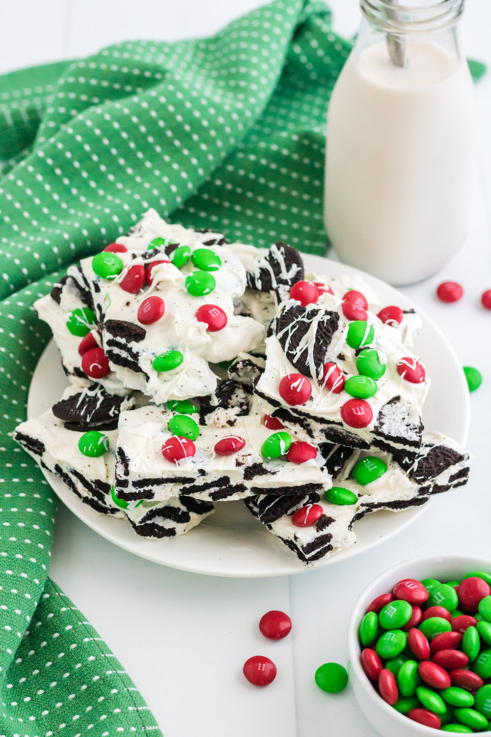Plate of holiday bark next to a green napkin, milk, and red and green M&Ms. 