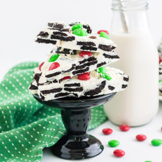 OREO bark with holiday M&Ms on a small black pedestal with more bark and candy on the table.