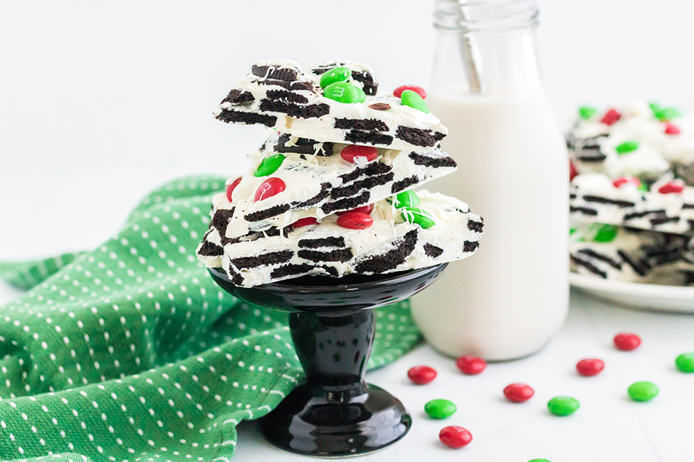 OREO bark with holiday M&Ms on a small black pedestal with more bark and candy on the table.