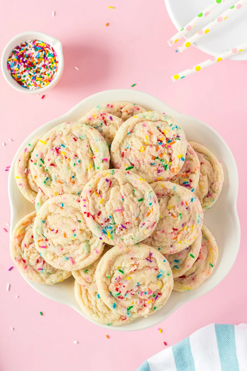 Plate full of funfetti cookies next to a bowl of sprinkles. 