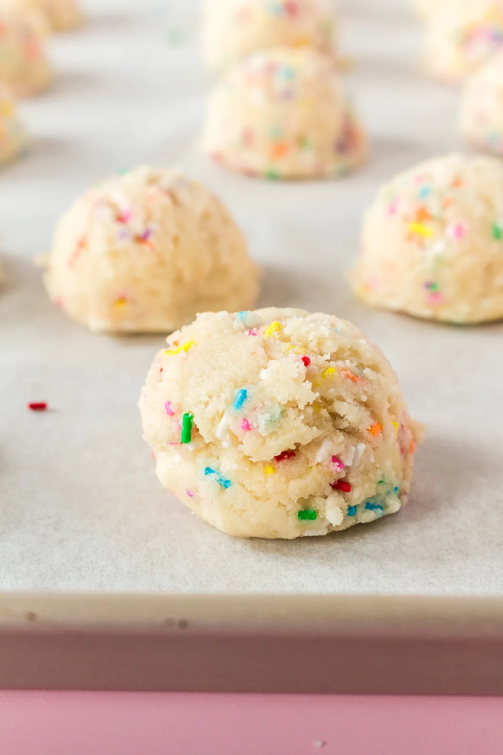 Sprinkles on top of cookie dough balls on a sheet.