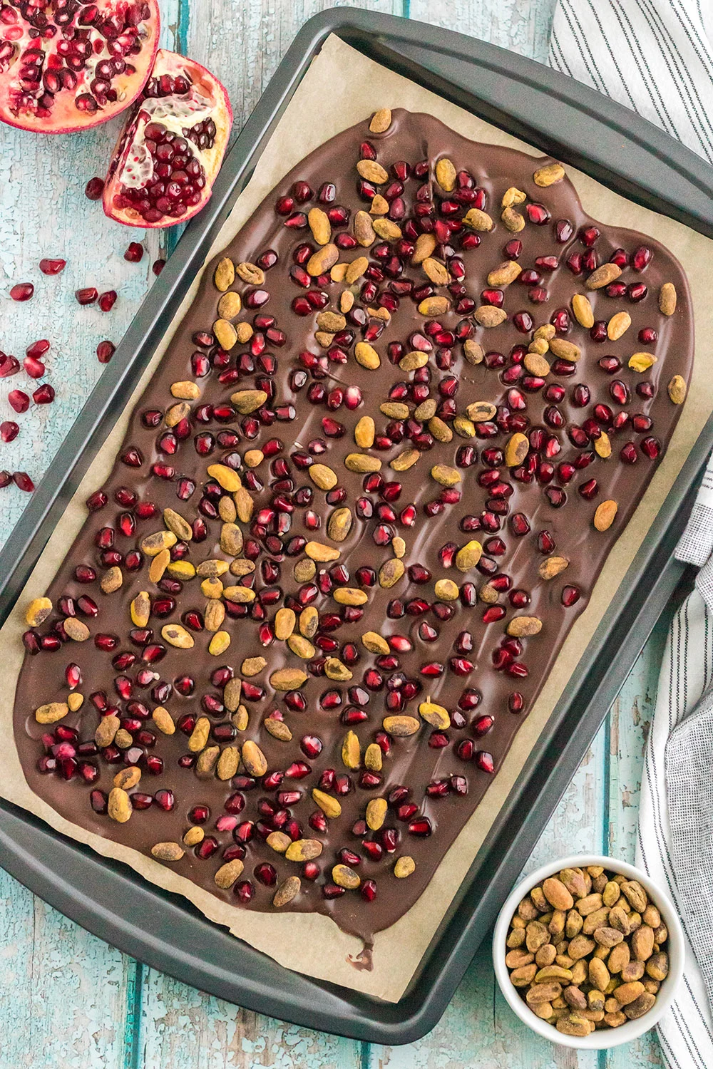 Chocolate bark in a baking sheet topped with pomegranate arils and pistachio nuts. 