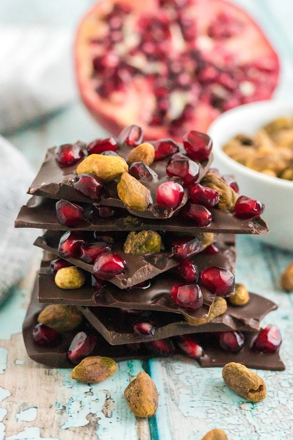 Chocolate pistachio bark pieces stacked with pomegranate in the background. 