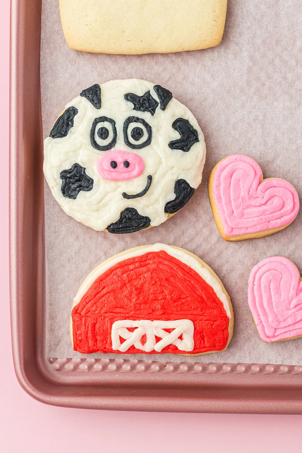 Cow, barn, and heart sugar cookies on a baking sheet. 