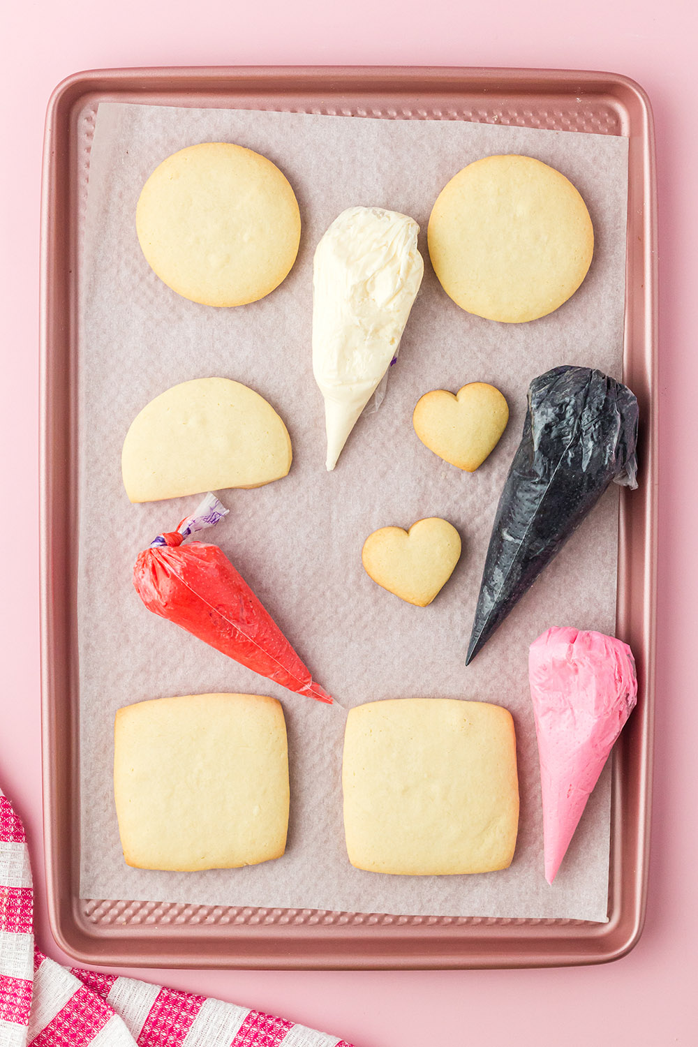 Cut out sugar cookies with bags of colored icing on a baking sheet. 