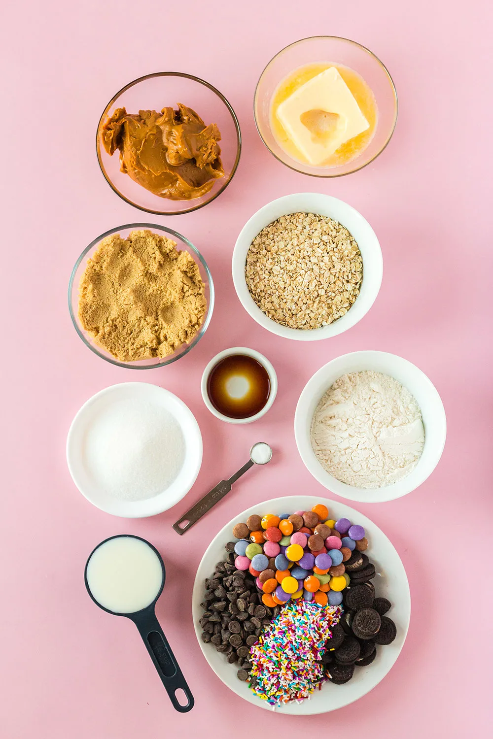 Butter, sugar, oats, and other ingredients in bowls on pink table. 
