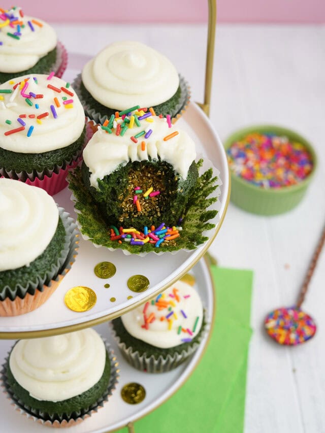 Cupcakes on a tray. One of them has a bite taking out showing the surprise filling of sprinkles.