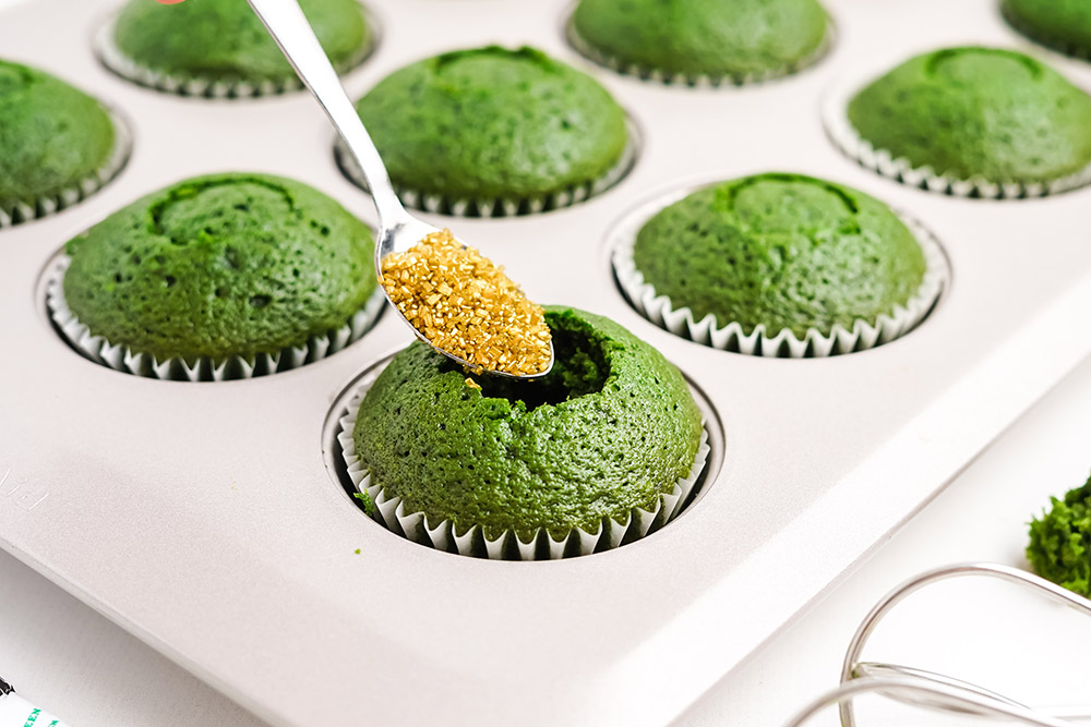 Spooning in gold sprinkles into green cupcakes for the filling.