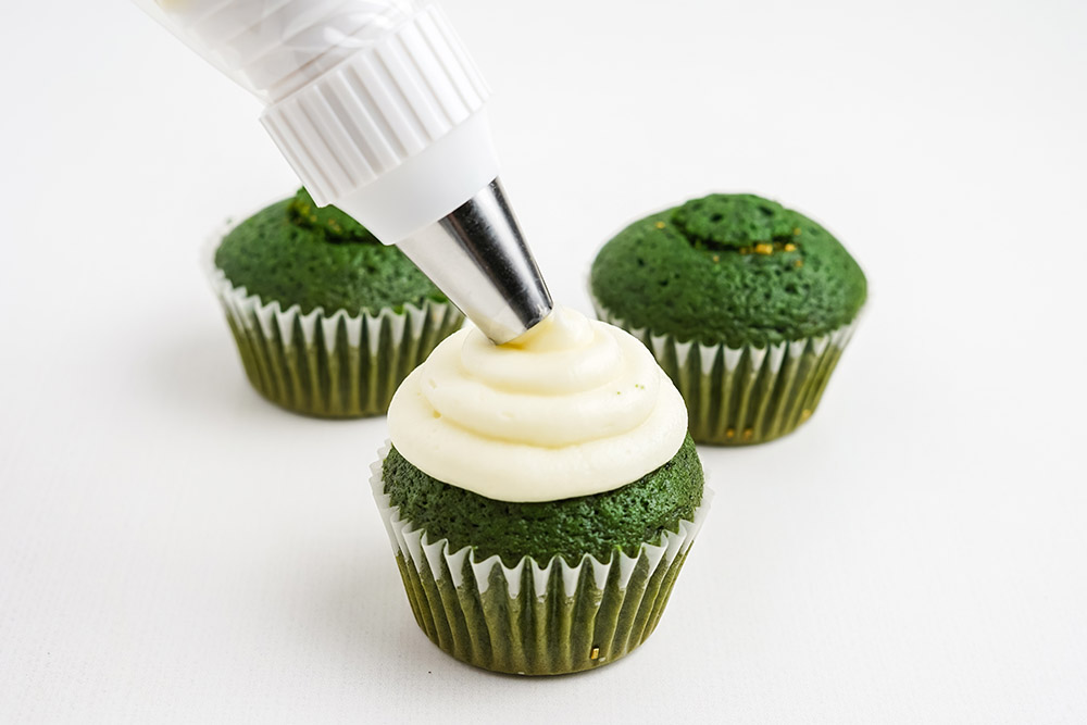 Piping white frosting onto green cupcakes.