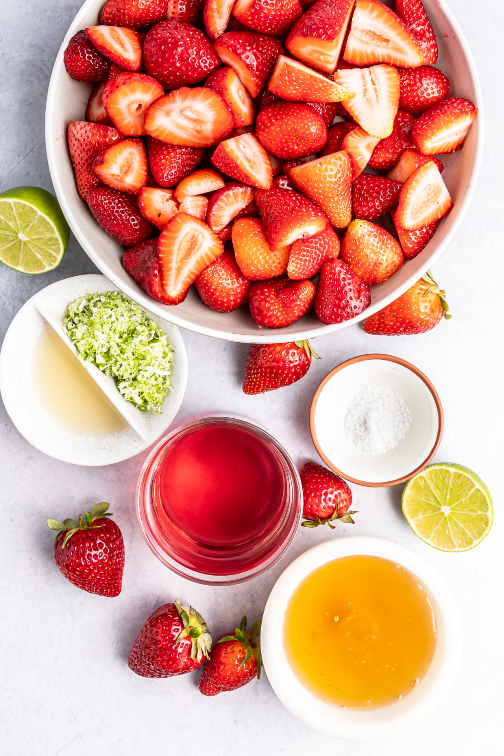 Strawberries, lime zest, sugar, and other ingredients for a granita in bowls. 