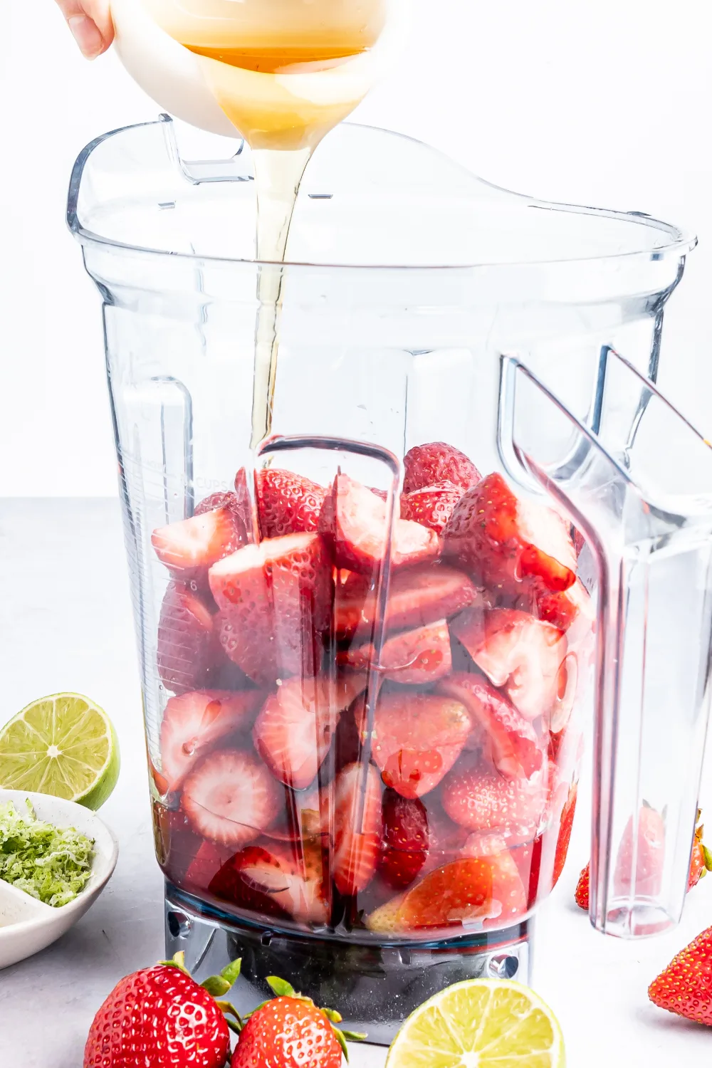 Pouring maple syrup into a blender with strawberries in it. 