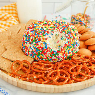 Cream cheese ball covered in sprinkles on a plate with pretzels, graham crackers, and cookies.