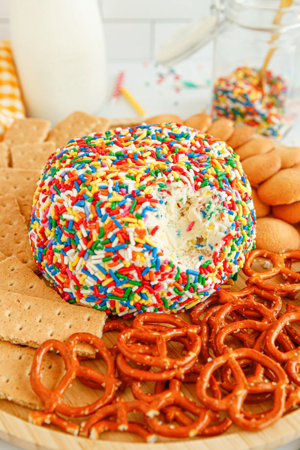 Cheese ball dip covered in sprinkles with pretzels and cookies around it. 