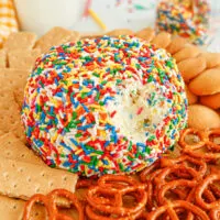 Cheese ball dip covered in sprinkles with pretzels and cookies around it.