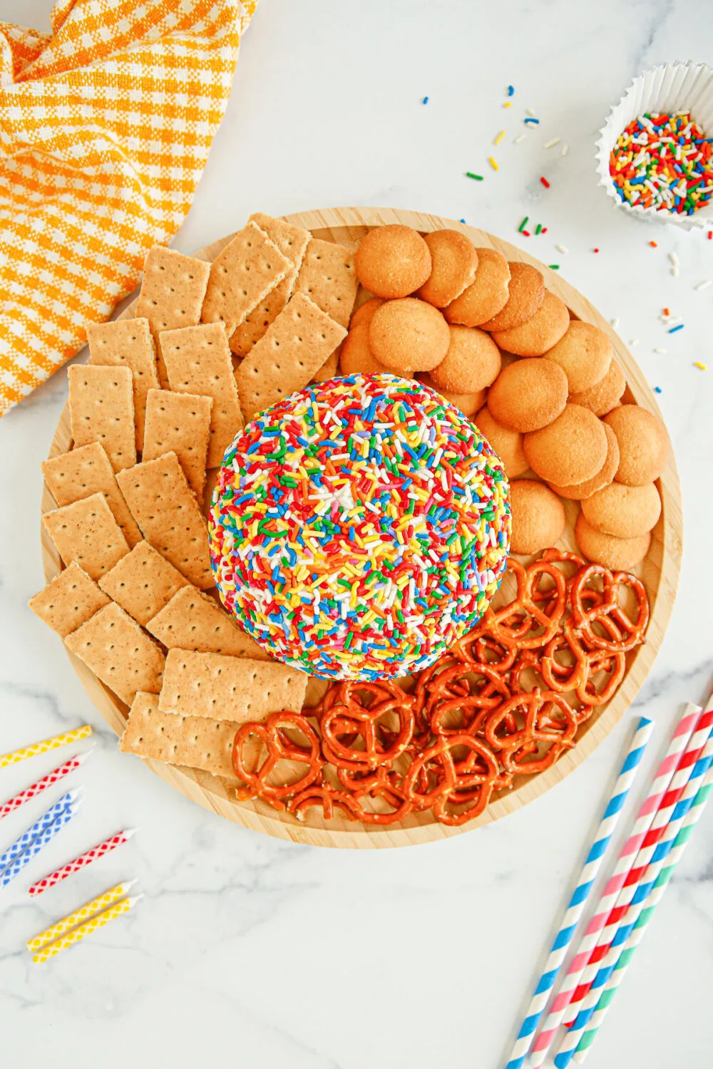 Funfetti cheese ball in the middle of a plate surrounded by pretzels, graham crackers, and nilla wafers. 