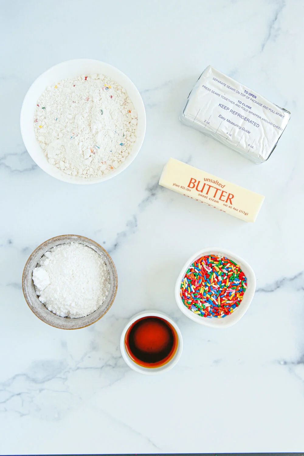 Cream cheese, butter, sprinkles, and other ingredients in bowls. 
