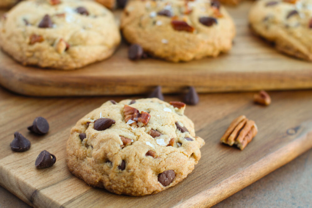 Chocolate chip cookies with pecans and flaky salt on boards. 