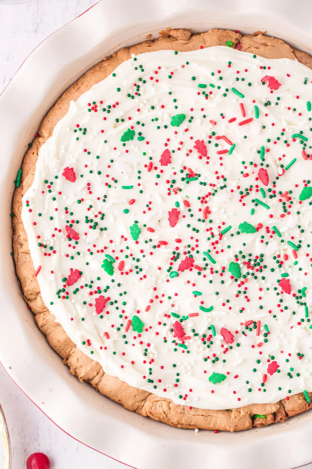 Cookie pie topped with frosting and red and green candies. 