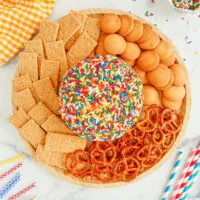 Funfetti cheese ball in the middle of a plate surrounded by pretzels, graham crackers, and nilla wafers.