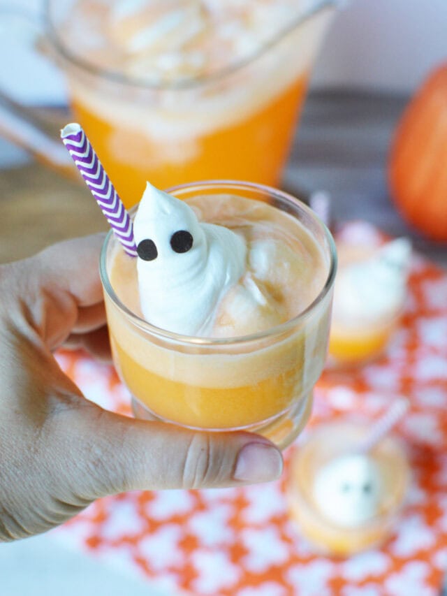 Holding a cup of orange ice cream punch with a ghost topping.