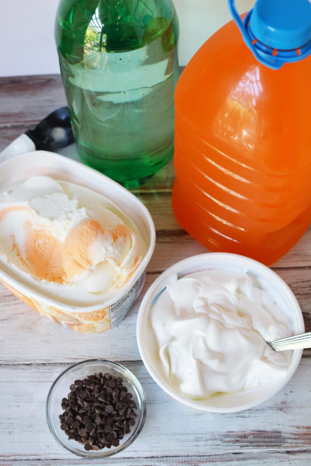 Lemon lime soda, orange drink, creamsicle ice cream, whipped topping, and chocolate chips on a table. 