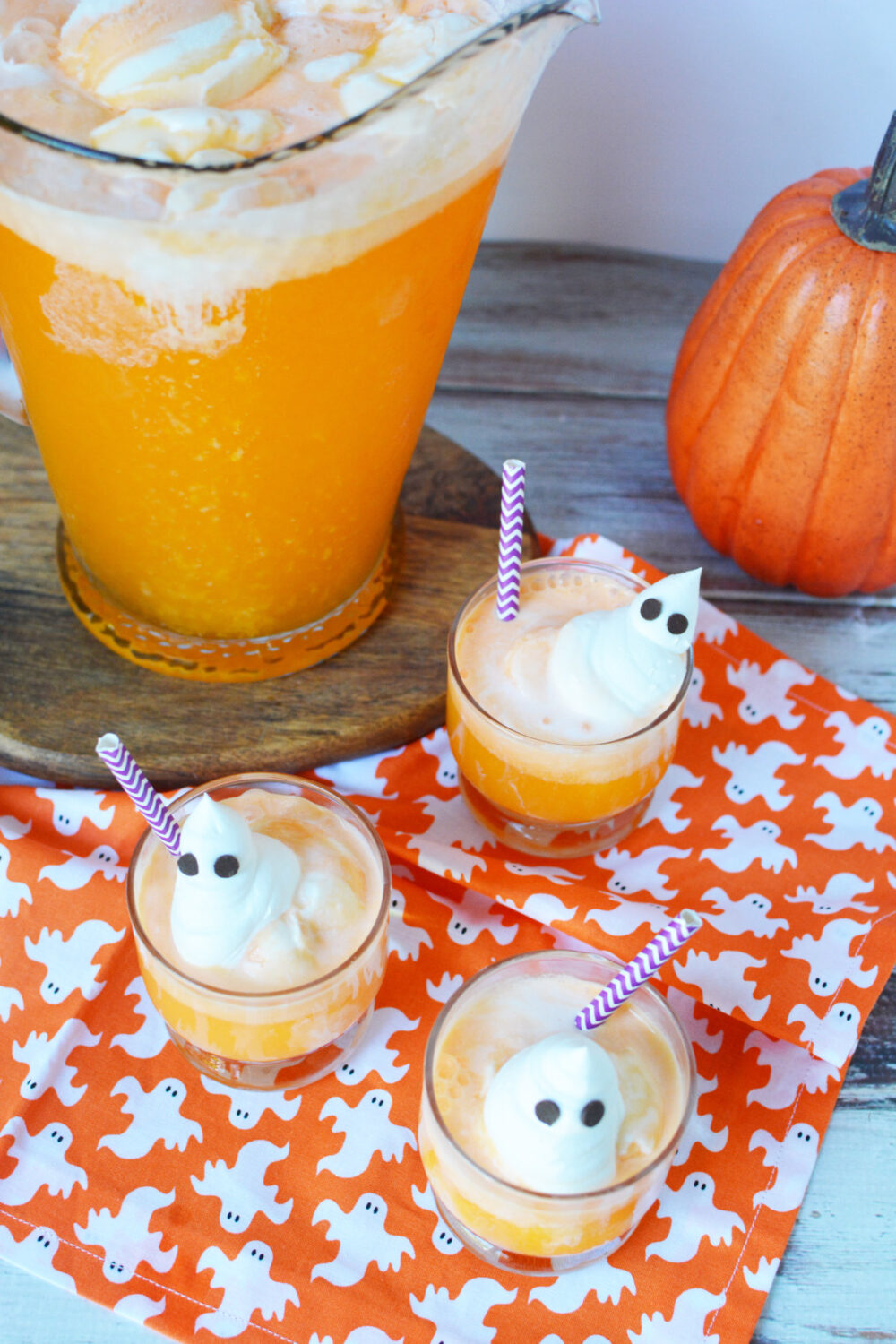 Three cups of orange creamsicle punch topped with whipped cream ghosts. 