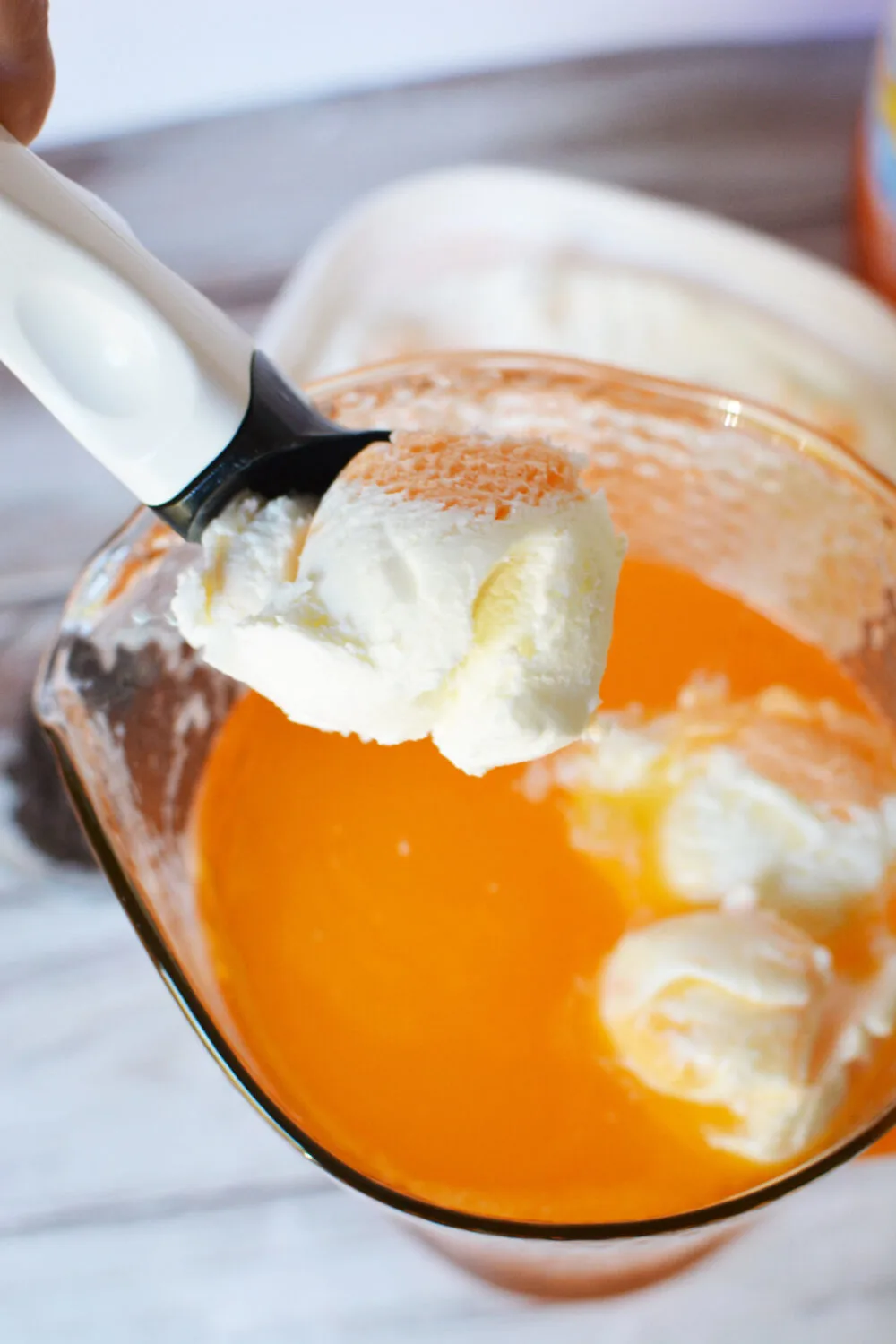 Adding ice cream to a pitcher with an orange drink in it. 