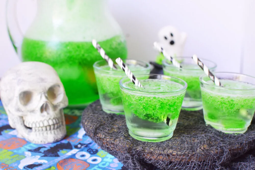 Glasses of green drink next to a pitcher and a skull decoration. 