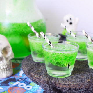 Glasses of green drink next to a pitcher and a skull decoration.