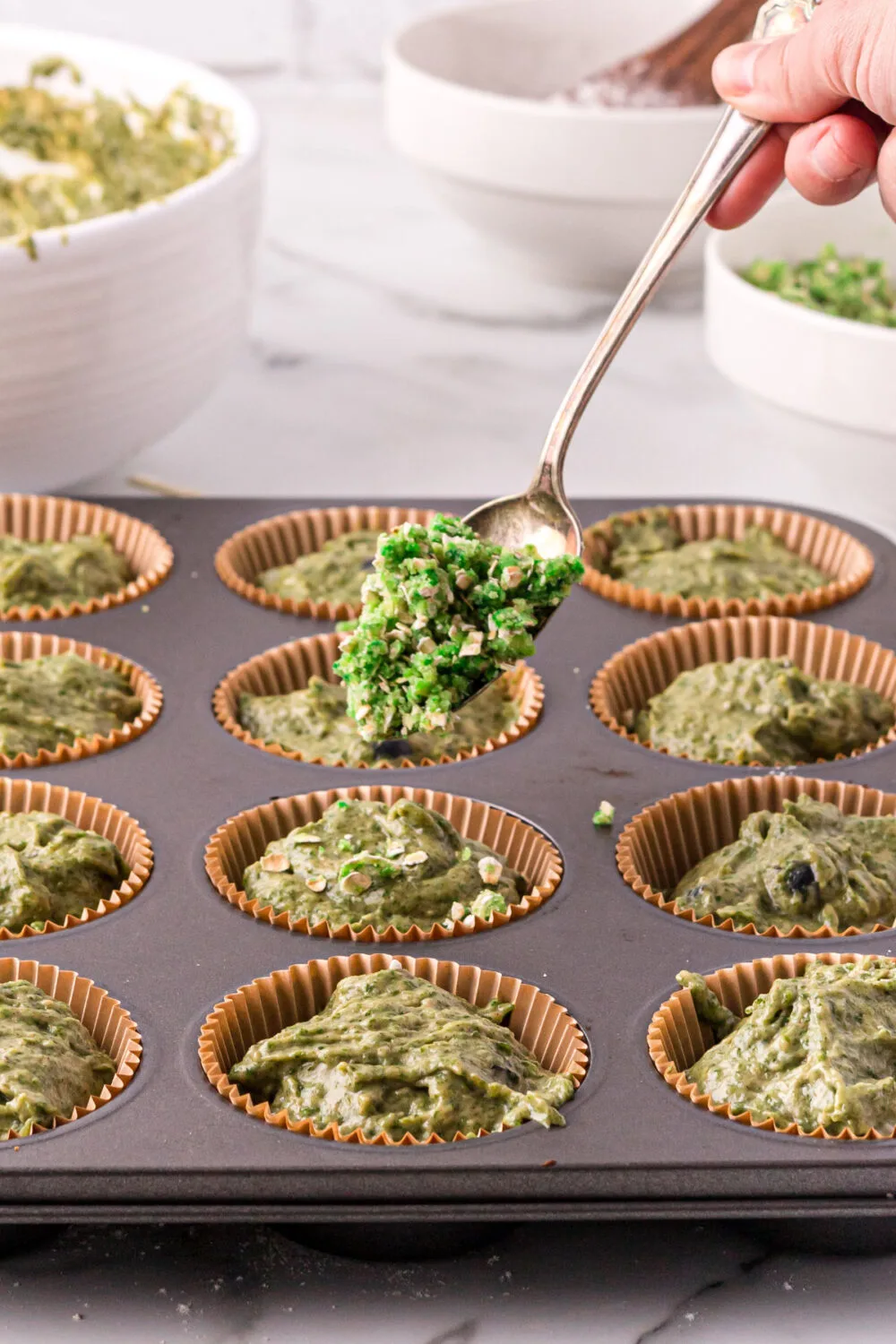 Topping muffins with green crumble in a muffin tin.