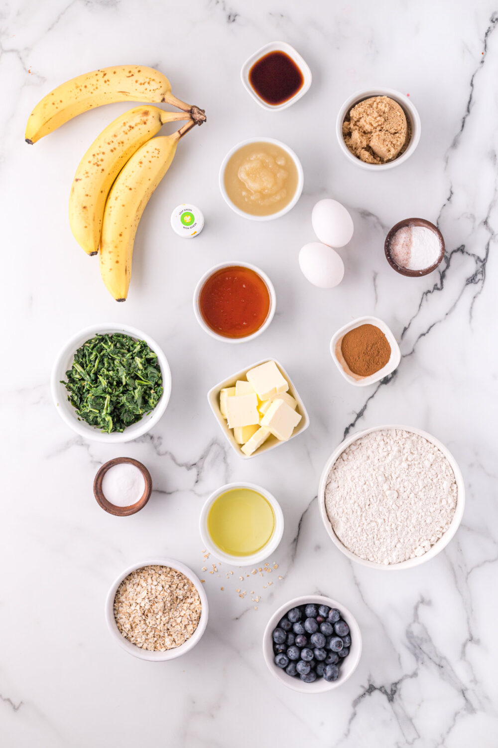 Bananas, spinach, blueberries, and other ingredients for muffins in bowls. 