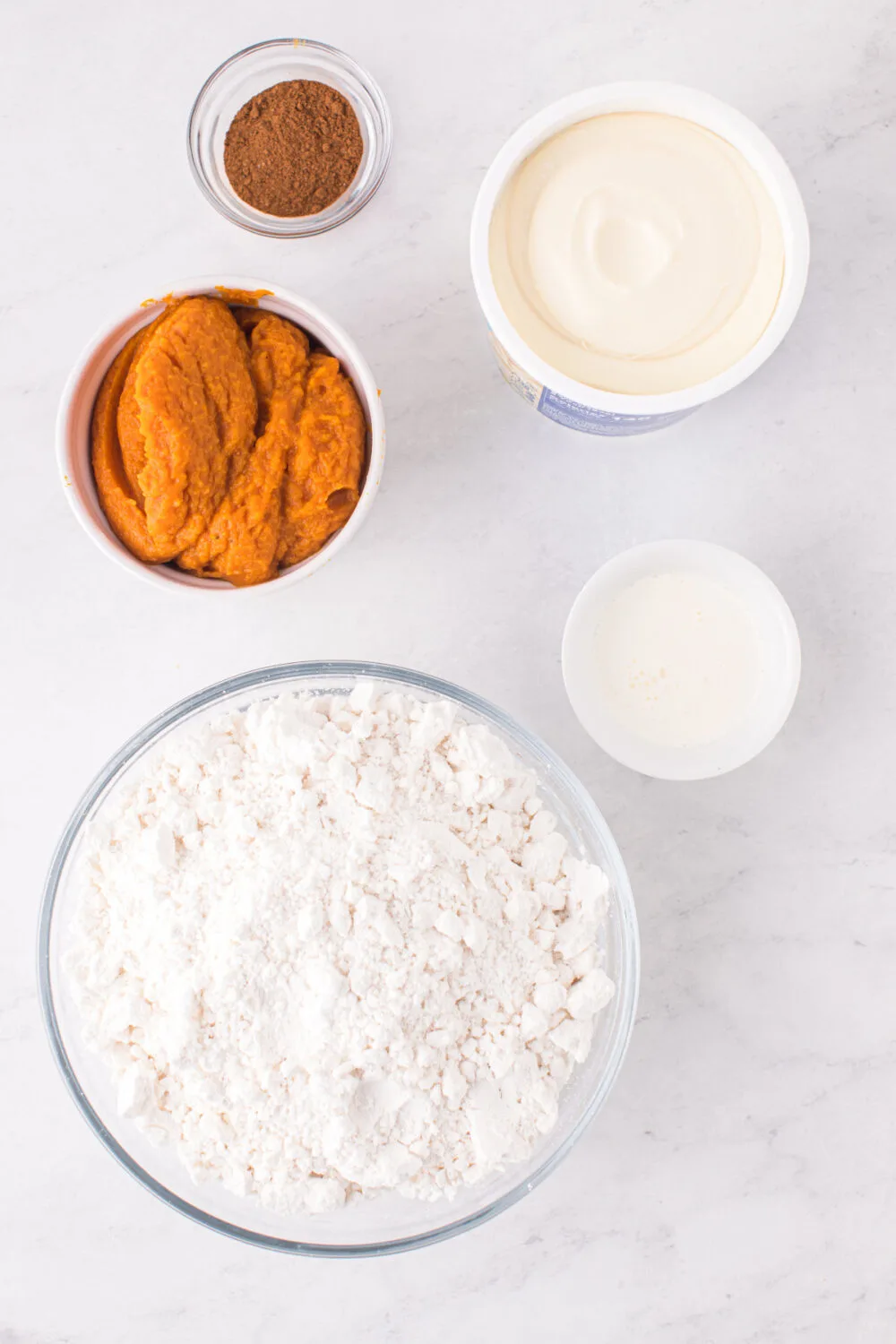 Pumpkin, flour, cinnamon, and other ingredients for pumpkin cookies in bowls.