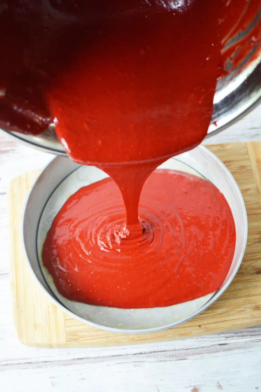 Pouring red velvet cake batter into a cake round pan.