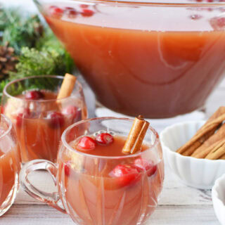 Mugs of punch with cranberries and cinnamon sticks next to the bowl of punch.