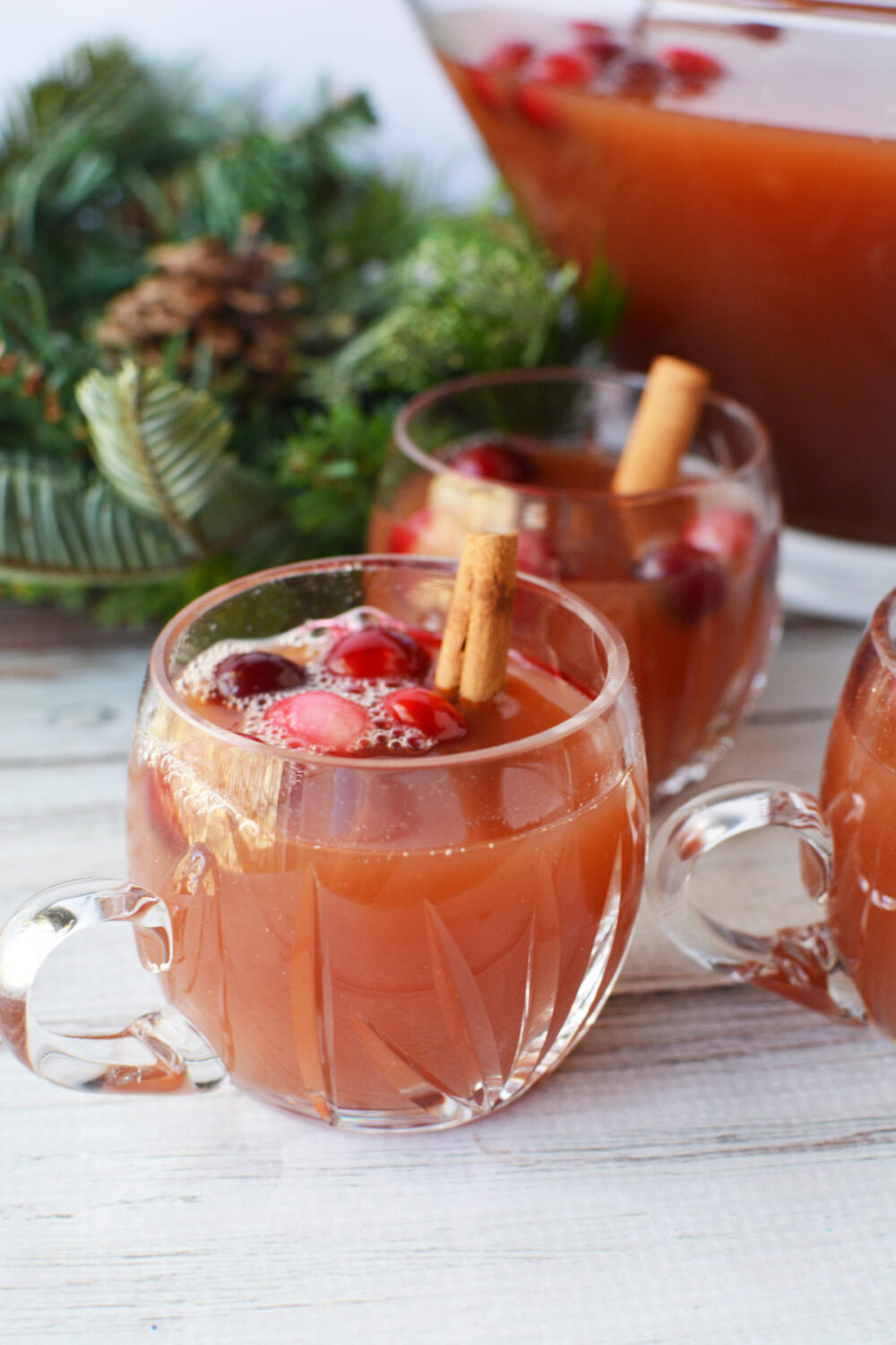 Clear glass of punch with cranberries and cinnamon sticks with holiday decor on the table. 